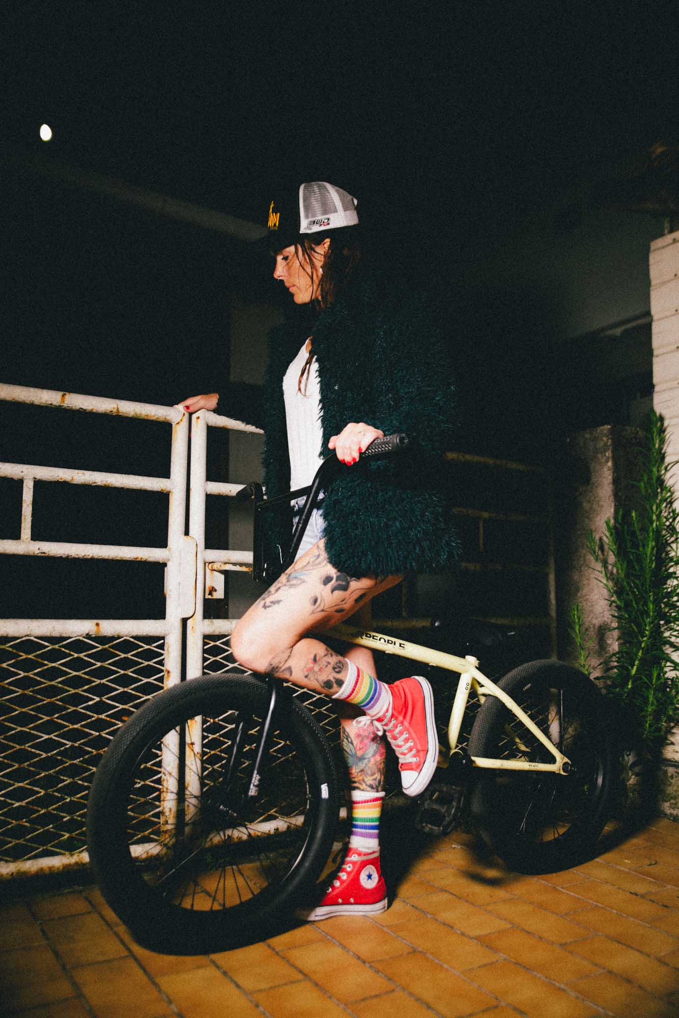 helene est sur un BMX de côté, elle s'adosse à un portail rouillé, photographie couleur