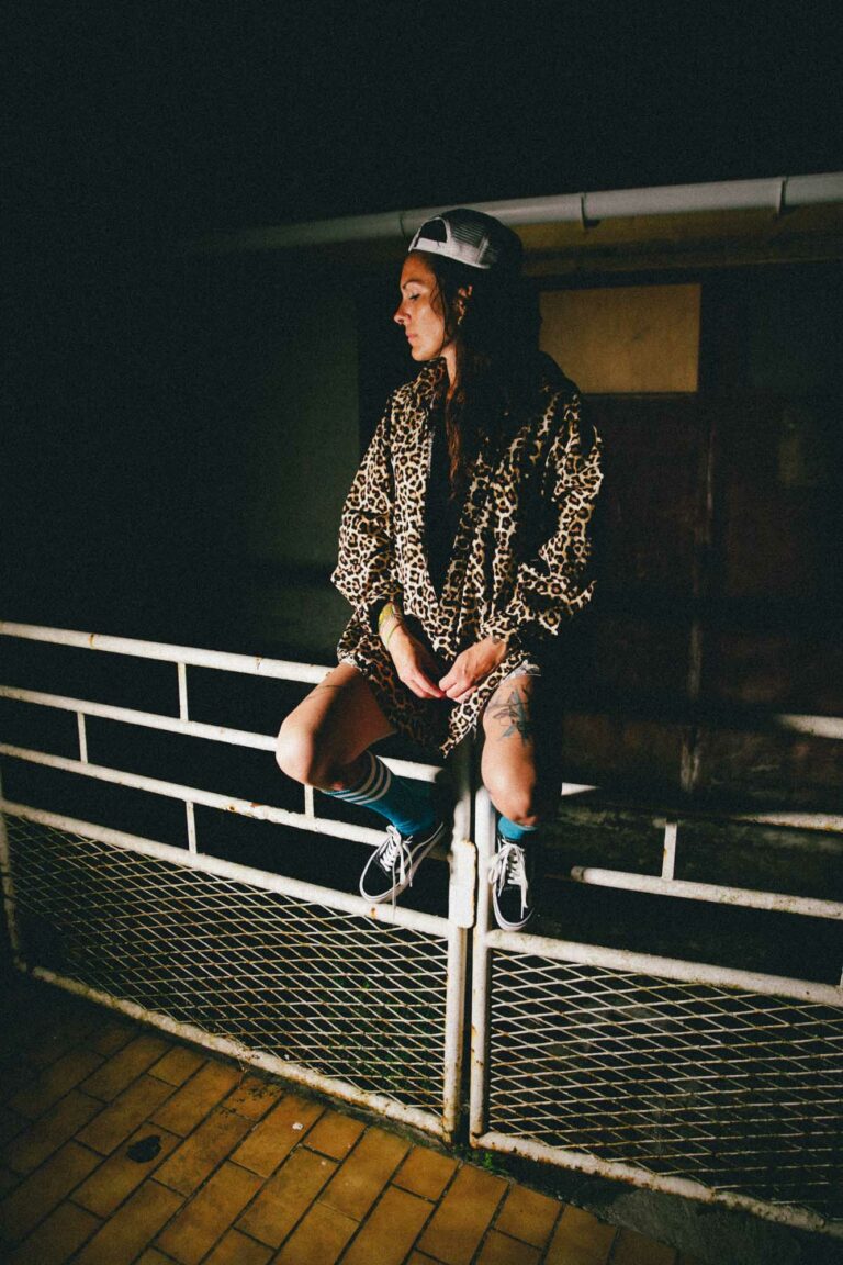 une femme est assise sur un vieux portail, elle est en short en jean avec un haut en loeopard, elle porte une casquette et donne un côte west coast à cette photographie couleur