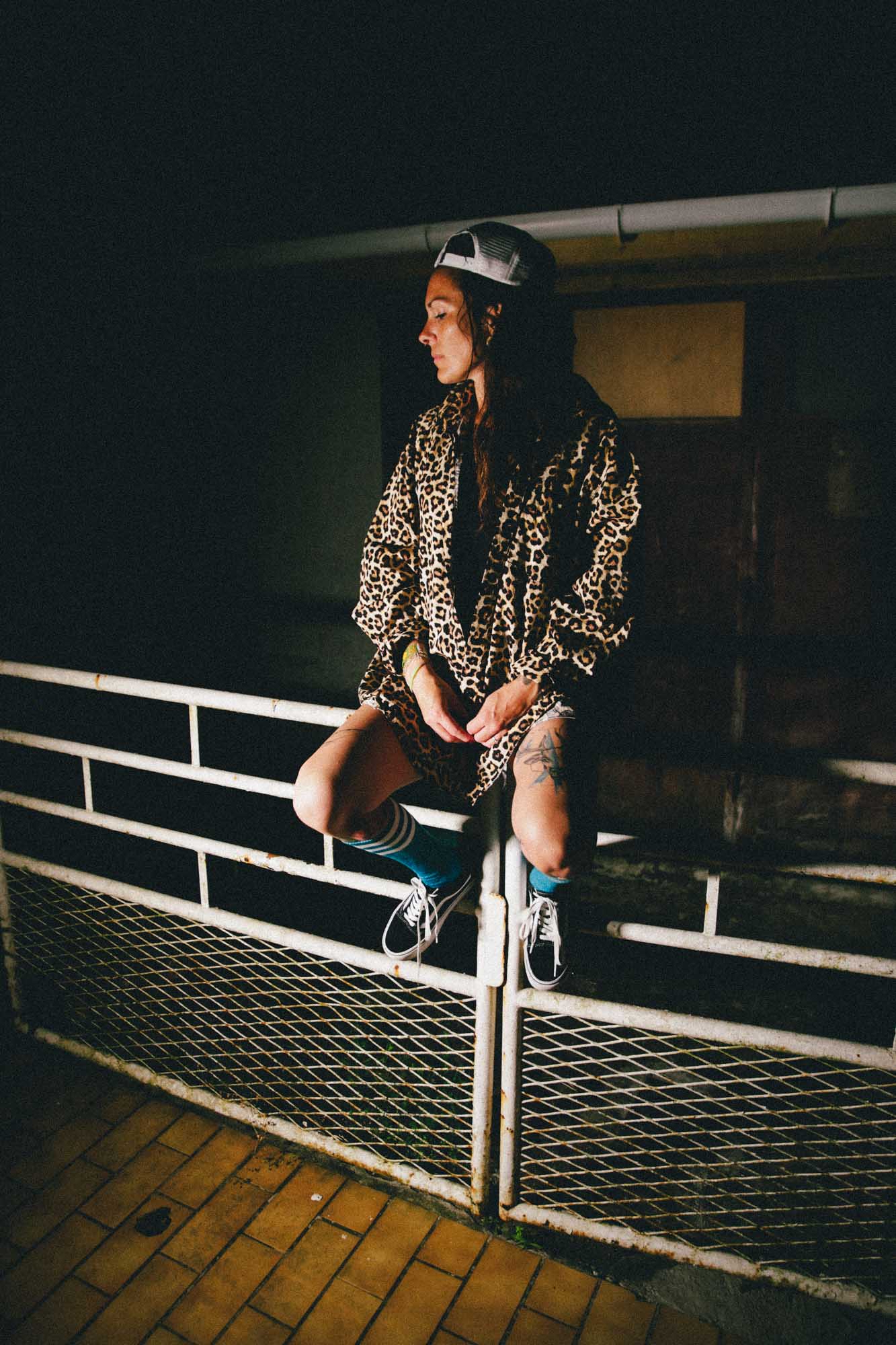 une femme est assise sur un vieux portail, elle est en short en jean avec un haut en loeopard, elle porte une casquette et donne un côte west coast à cette photographie couleur