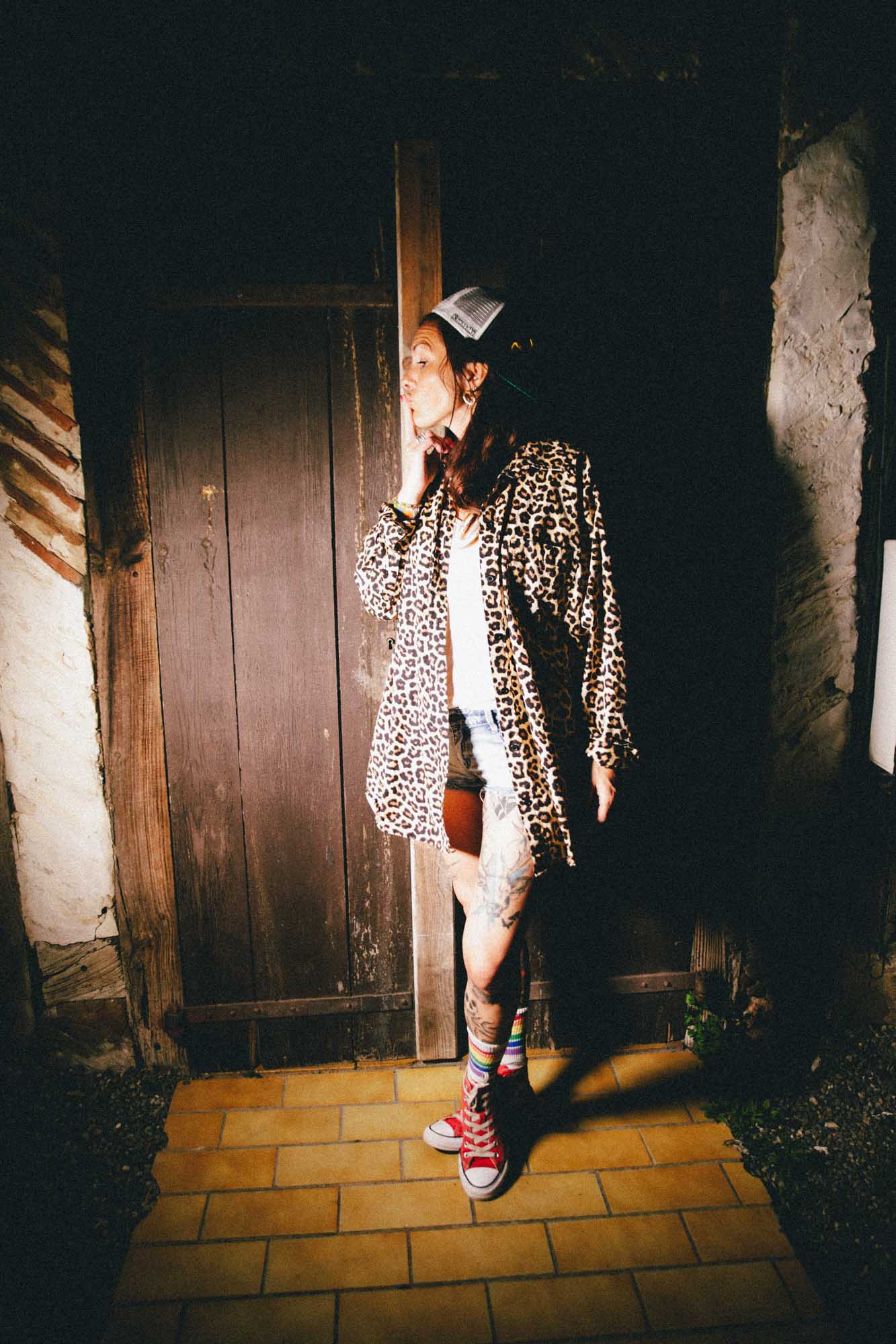 une jeune femme en converse et chaussettes americaines se porte de profile avec un haut leopard et une casquetten elel pose ses doigts sur sa bouche