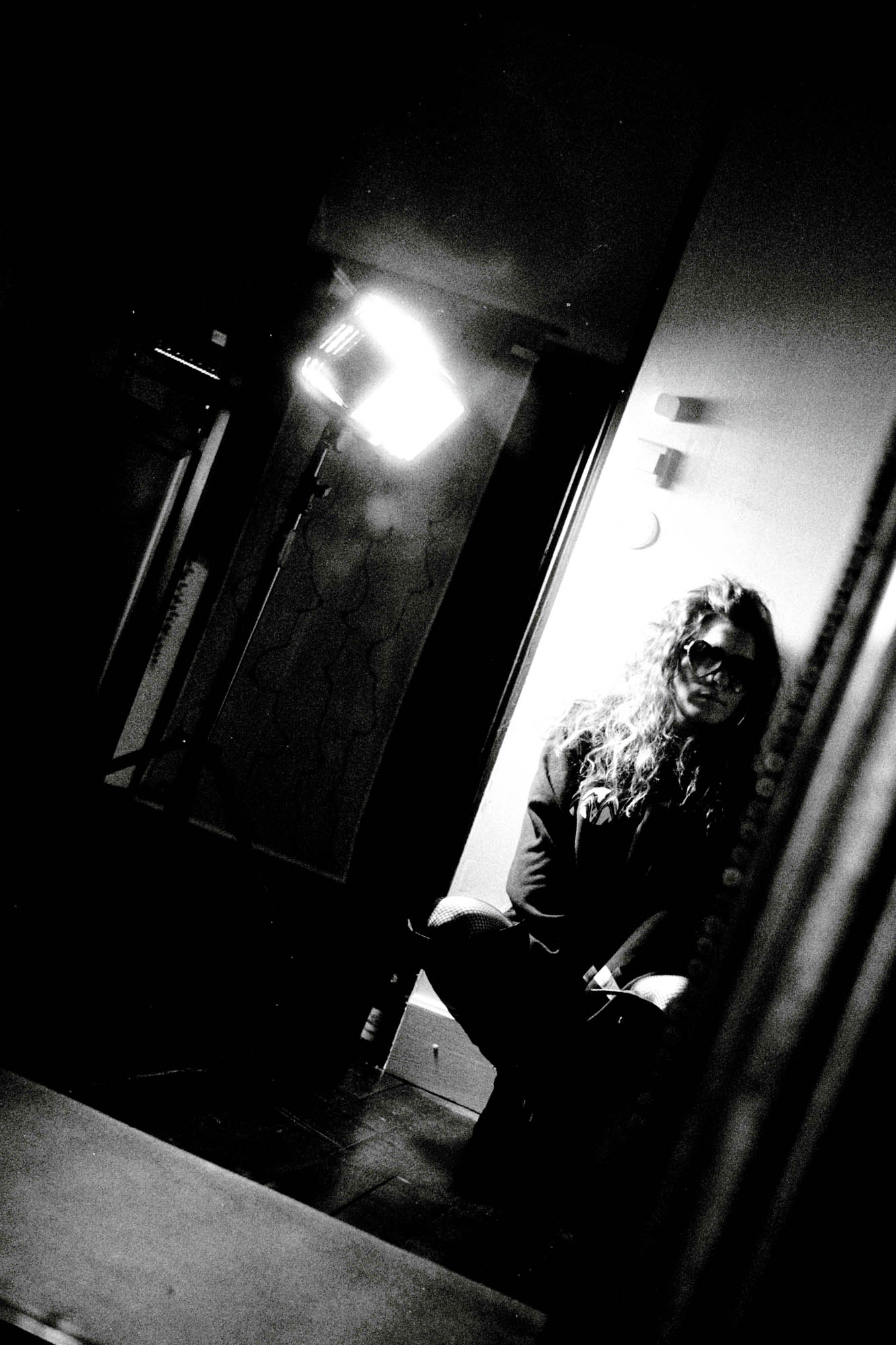 une femme assise dos au mur regarde de travers à côté d'une lumière artificielle, photographie argentique en noir et blanc