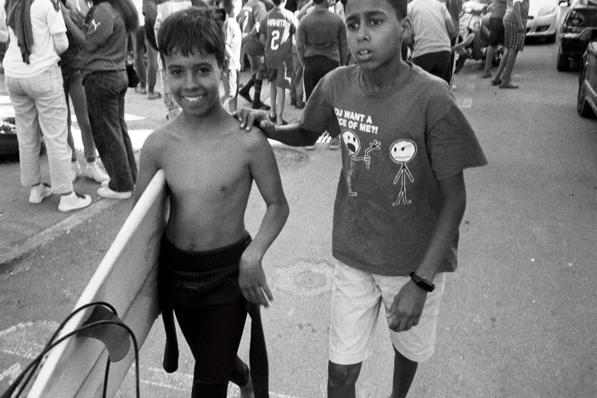 couple d'enfant marocains en noir et blanc argentique dont l'un porte sa pla,che de surf et me sourit pendant que l'aure tente de discuter