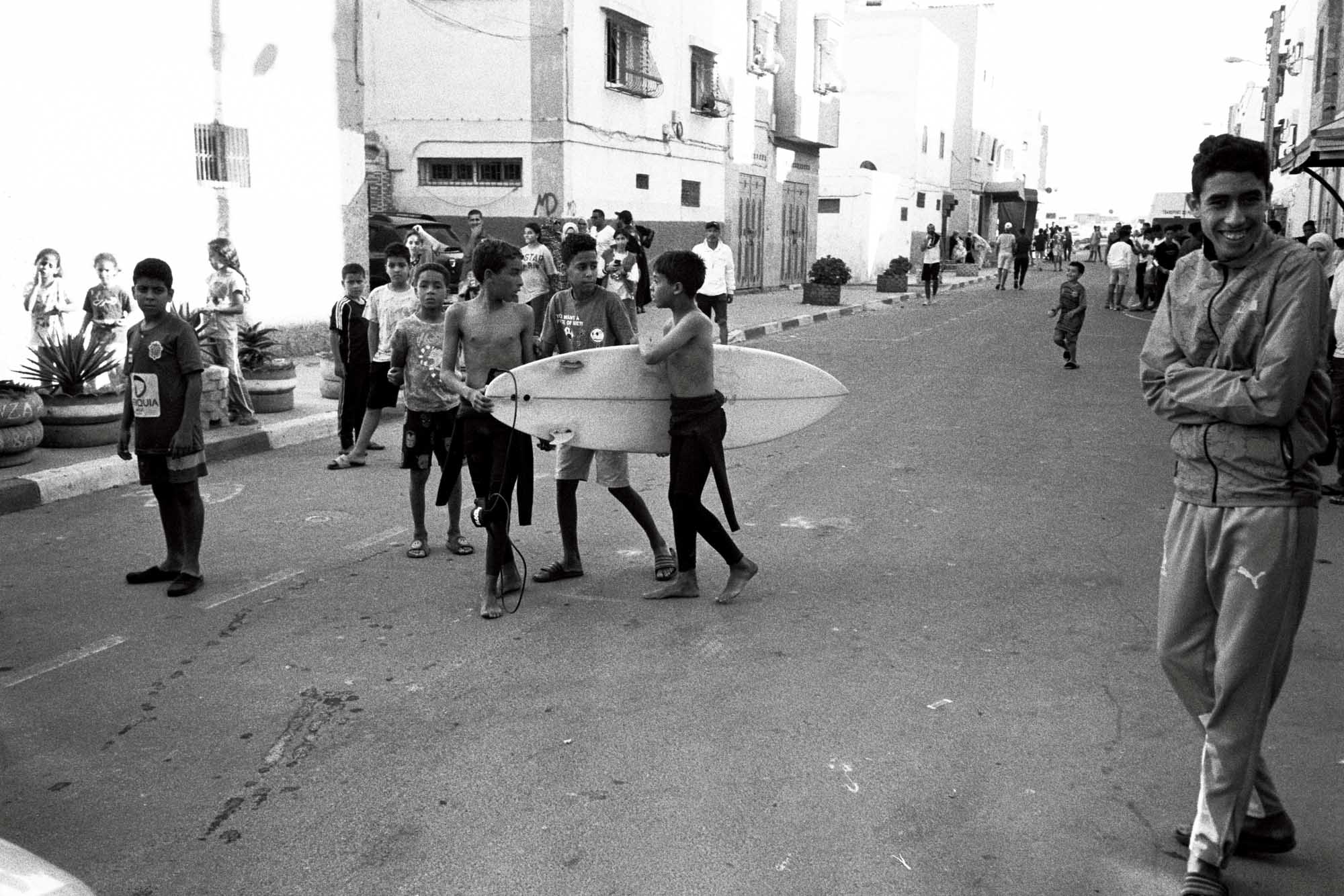 scène de vie marocaine avec un jeune qui porte sa planche et qui parle à d'aurtes au milieu de la route pendagt que la foule se presse