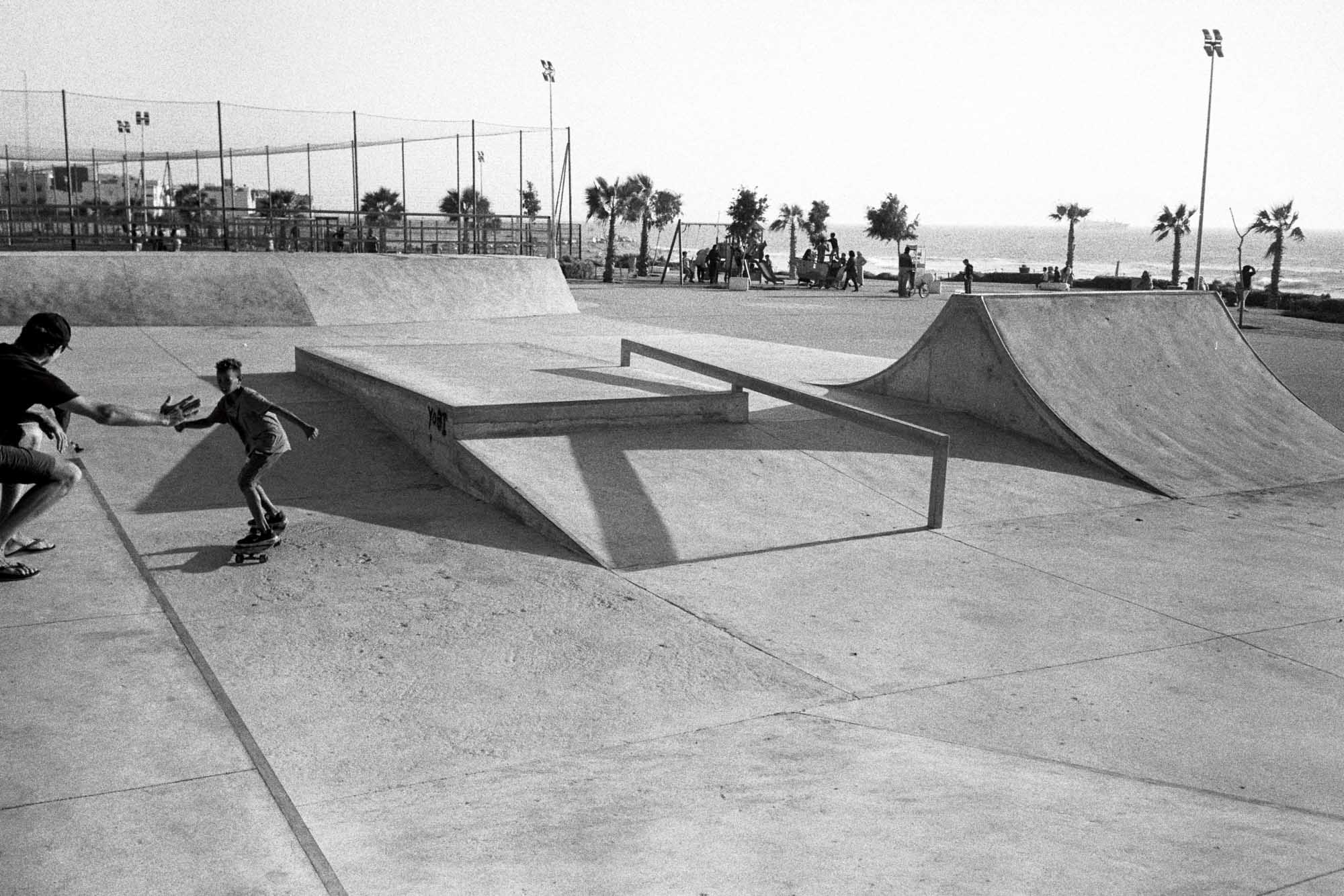 skatepark au maroc en bord d'océan avec sur le coté un jeune enfant qui apprend à skater et qui tape dans la main d'un adulte pendant qu'il roule