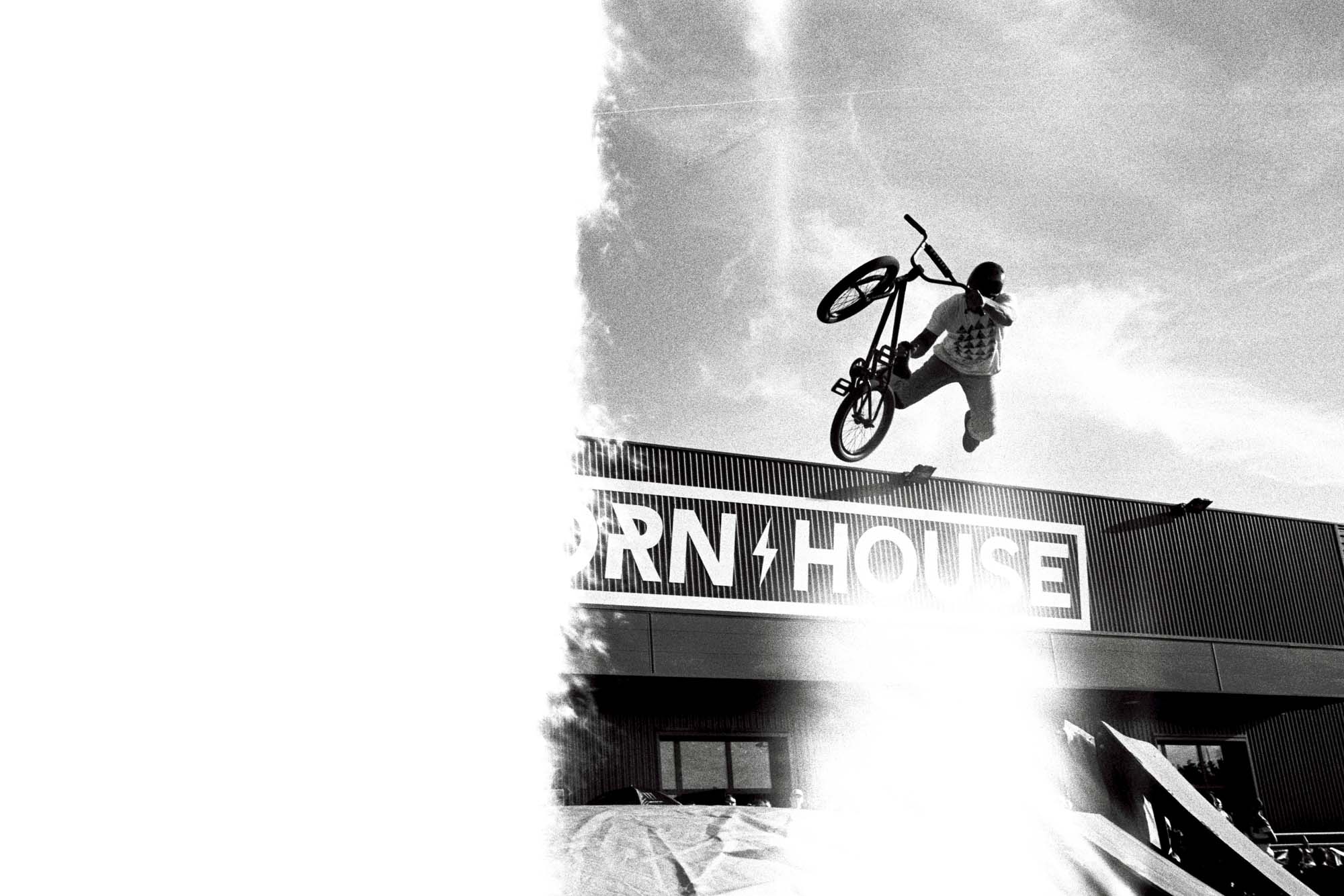 un rider en BMX effectue un saut avec son BMM en noir et blanc, la pellicule argentique a un raté avec une bande blanche sur la partie gauche