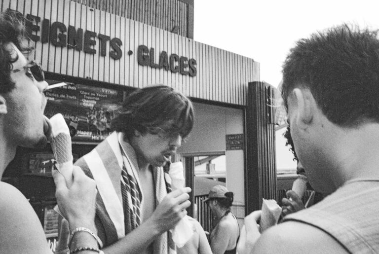 photo argentique d'un groupe de jeunes garçons qui mangent uneglace face à un snack, un adolescent a la bouche ouverte et lèche la glace - photographie en noir et blanc