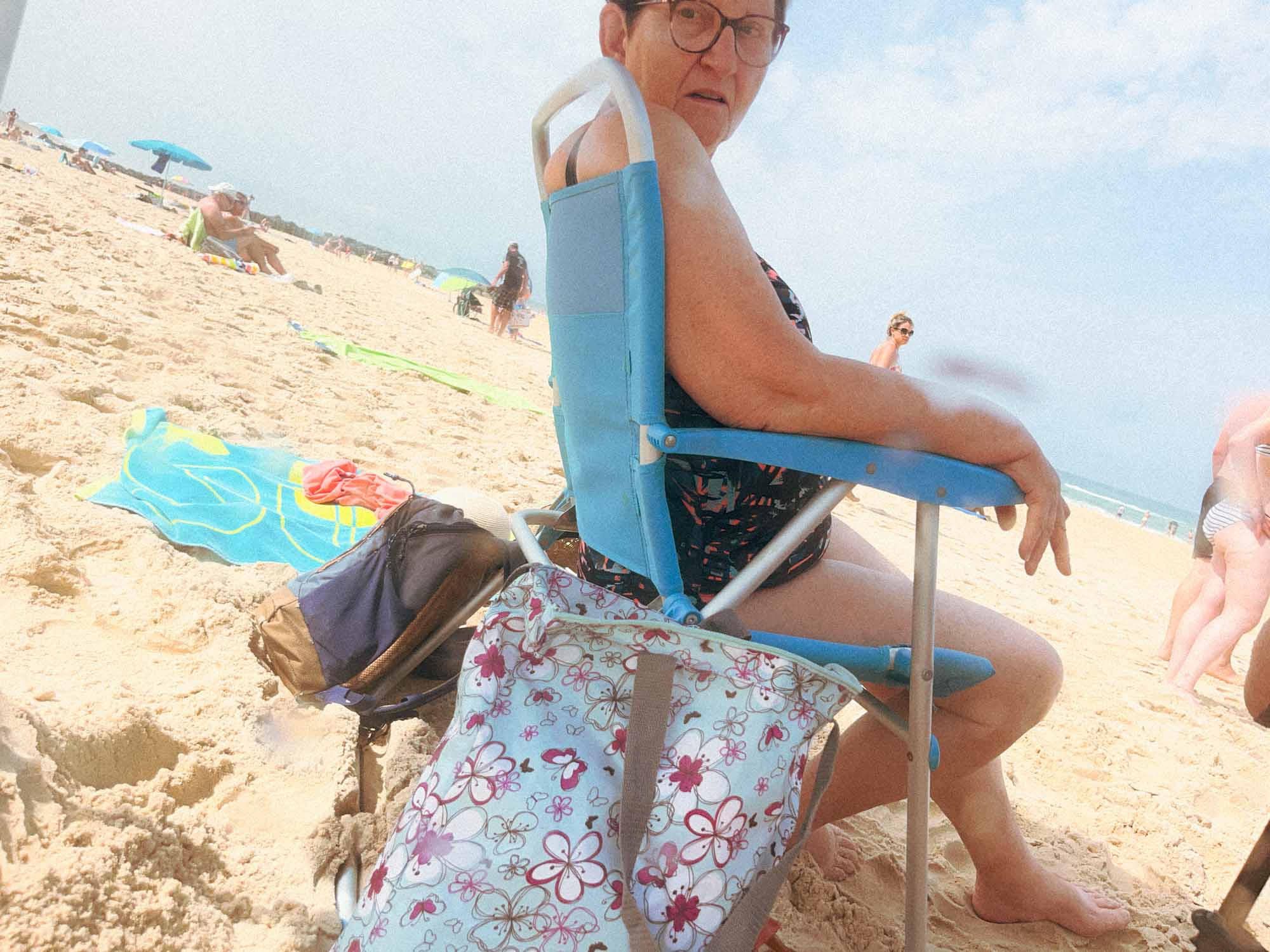 Une dame me regarde de près alors que le prends en photo, elle est assise sur une chaise de camping sur le sable