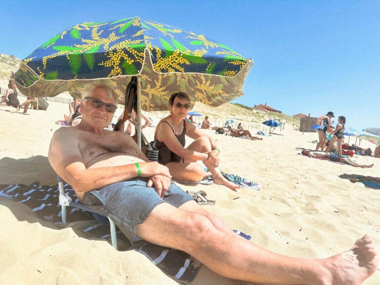 Photo couleur représentabnt un couple agé de touristes sous un parasol en maillot de bains et qui me regardent prendre la photo