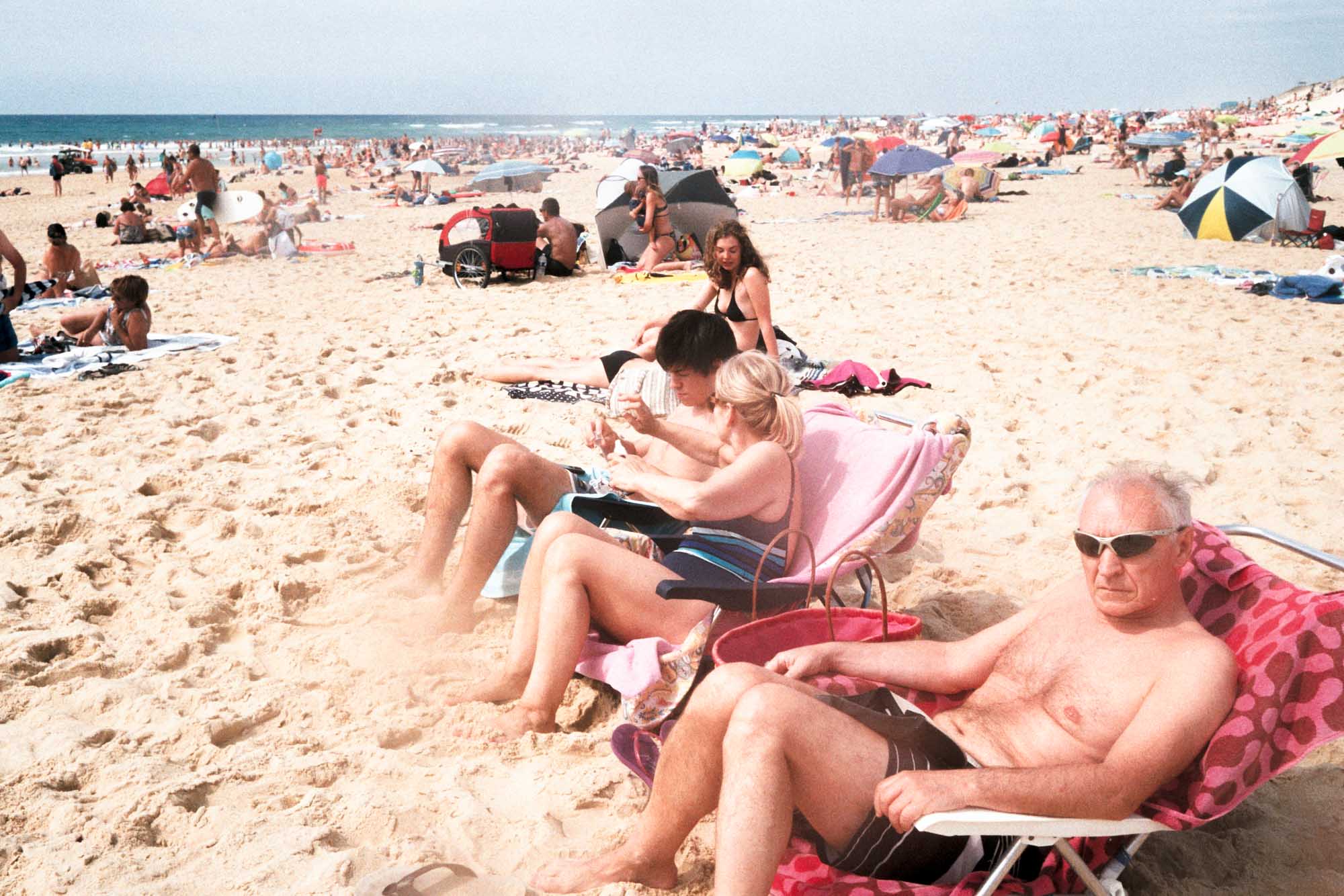 des touristes remplissent la plage de la centrale, on peut voir en premier plan un homme qui me regarde le prendre en photo , il est en dessous de moi torse nu et assis sur une chaise de camping