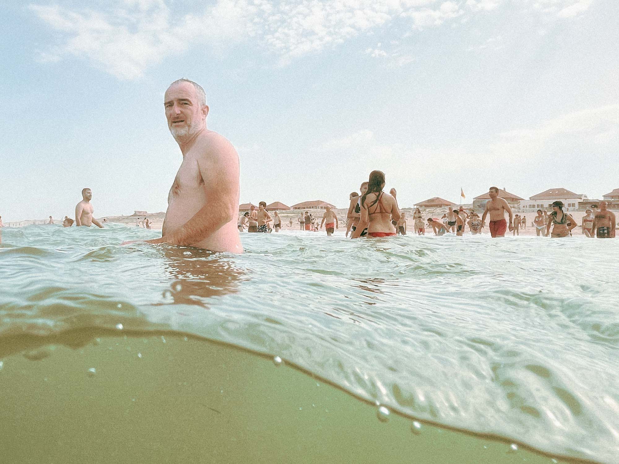 un homme est torse nu et me regarde le prendre en photo alors qu'il se baigne tranquille devant une foule de touristes