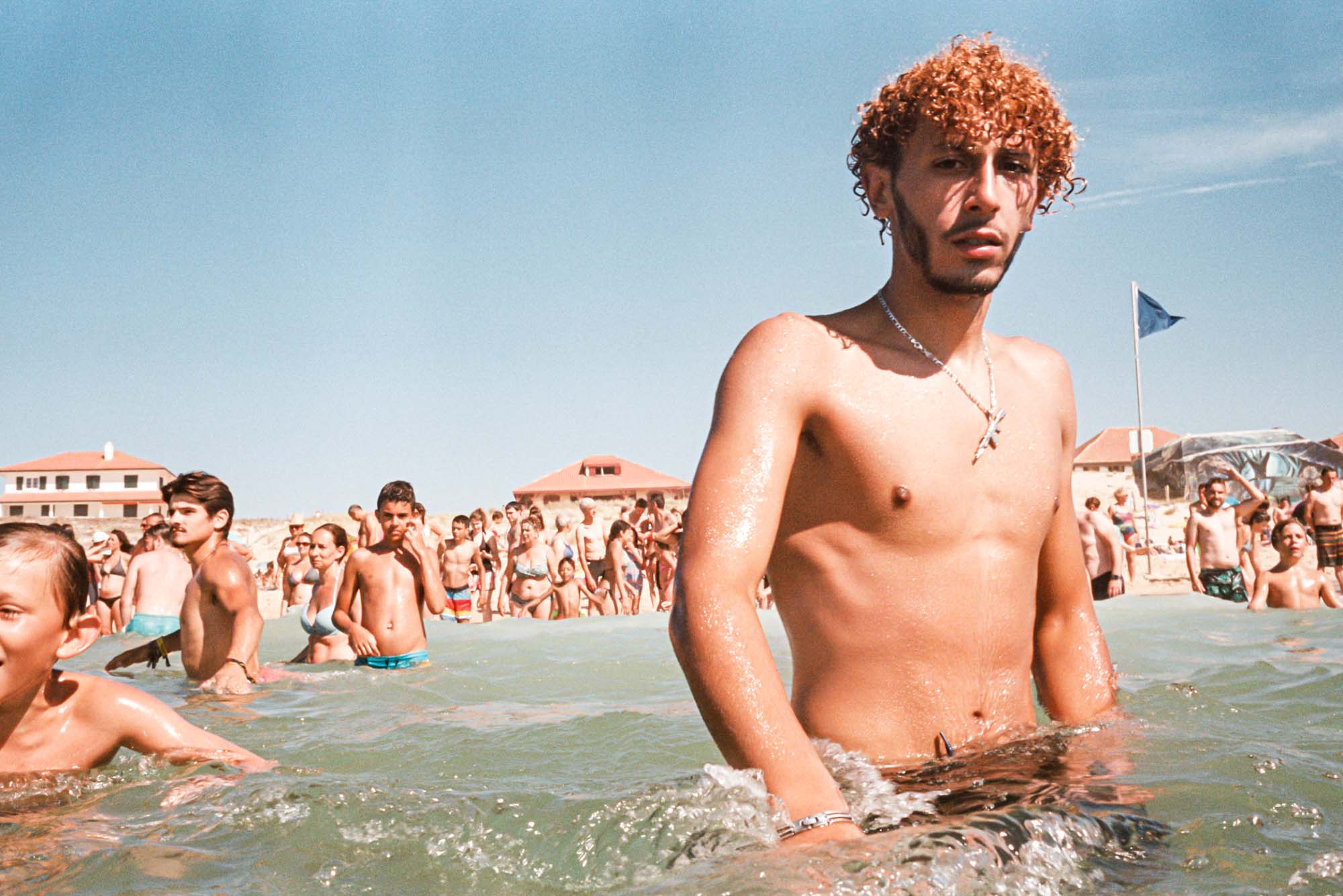 un jeune homme me regarde de près , il se baigne et porte une châine en pendentif avec une mitraillette en or