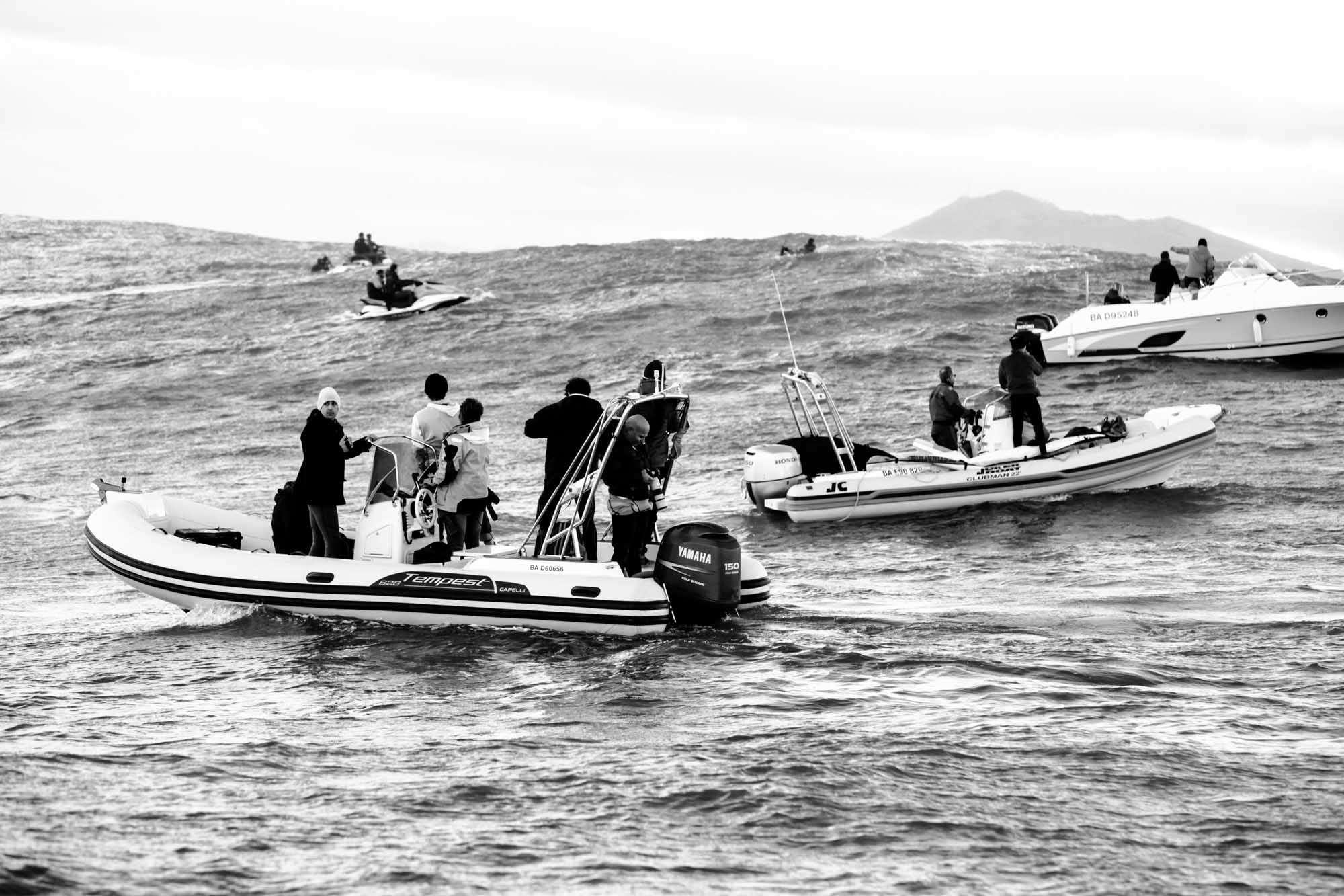 photographie noir et blanc des bateaux qui se positionnent pour prendre les photos de la vague de belharra, il y a du monde et ils ont des appareils en main