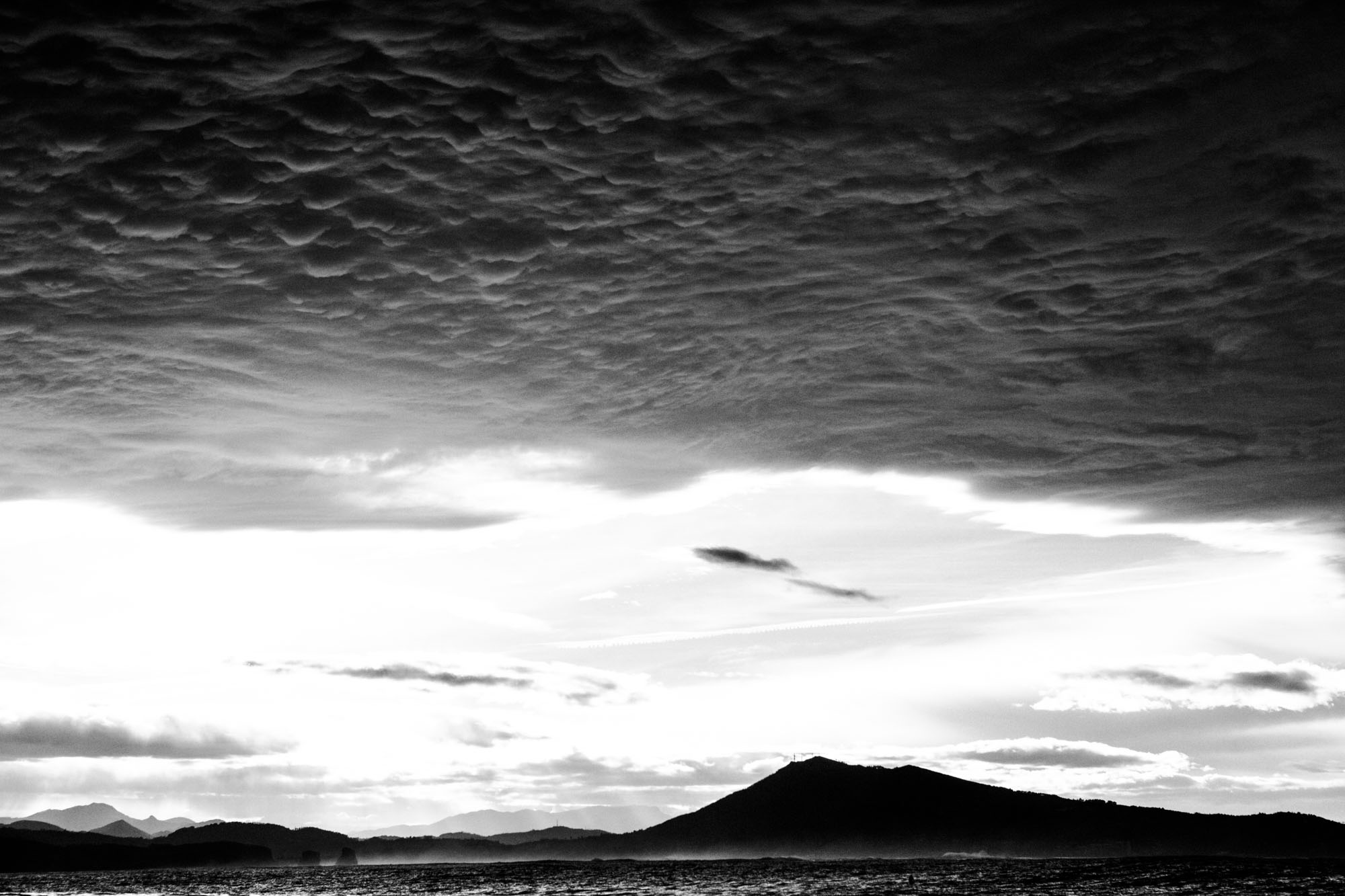 photographie de paysage en noir et blanc de la rune au pays basque et de nuages dans le ciel qui forment un plafond noir donnant un air grave