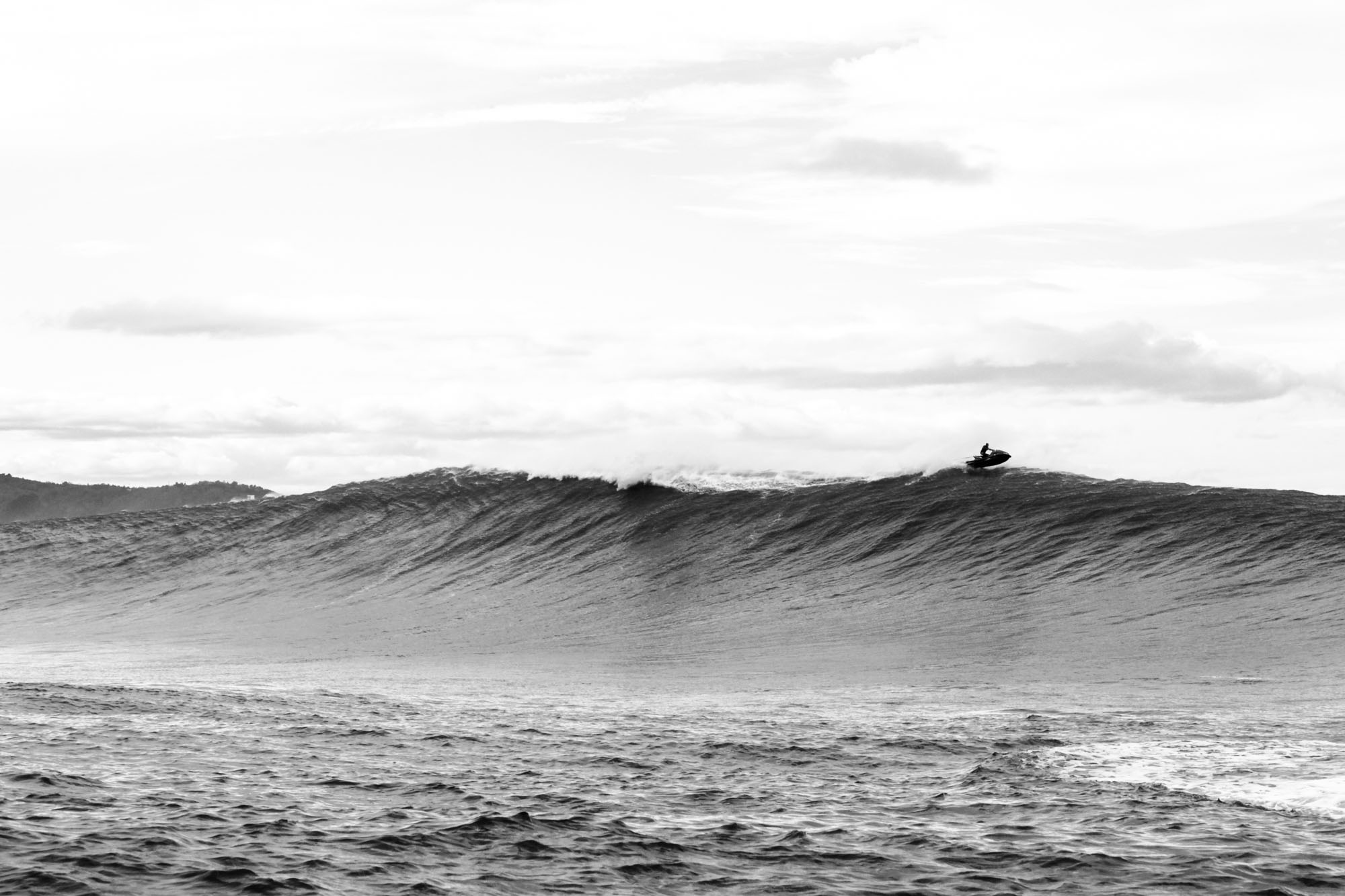 une vague en noir et blanc forme un mur, un jet ski est au dessus et semble longer la crête