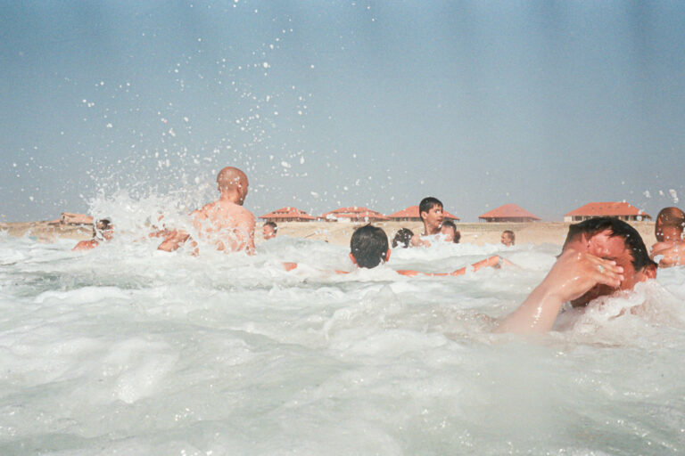 photographie argentique estivale en couleur , on voit juste des têtes qui sortent de l'eau et l'océan qui mousse