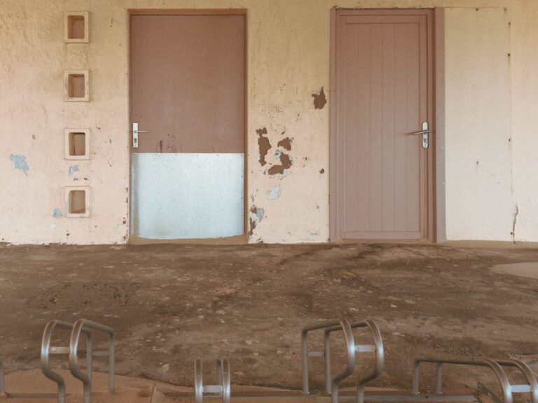 photographie couleur avec un porte vélo en premier plan et deux portes abimées ainsi qu'un mur décrépi dû aux intempéries