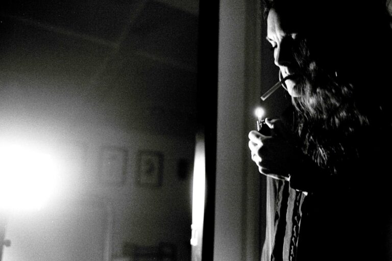 une femme allume une cigarette en intérieur, dans un décor noir te blanc