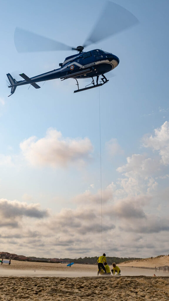 Hélicoptère de la gendarmerie en vol, câble de treuil tendu vers l'équipe au sol