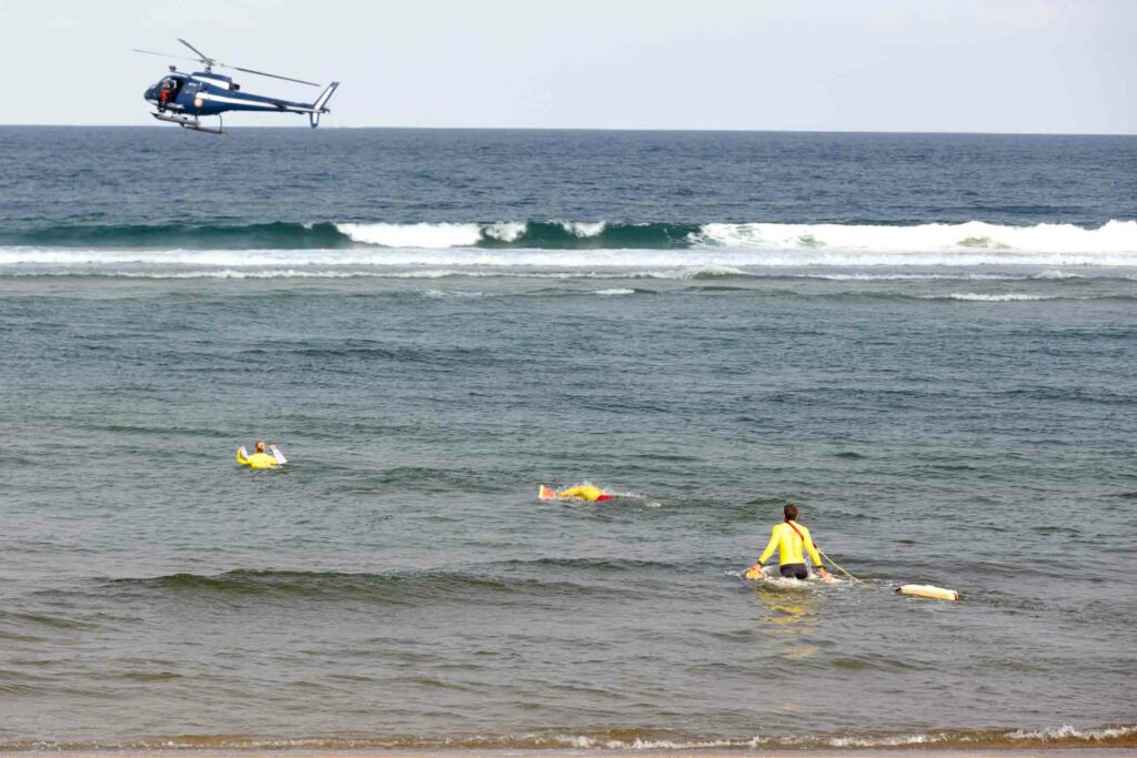 Nageurs-sauveteurs en mer encadrant un exercice de sauvetage, hélicoptère en vol au-dessus des vagues