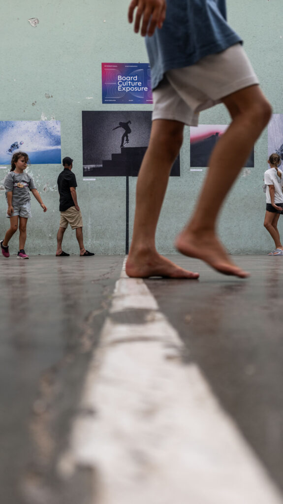 Jambe d'un jeune visiteur au premier plan, tirages exposés au Mur à Gauche en fond, Board Culture Exposure Biarritz