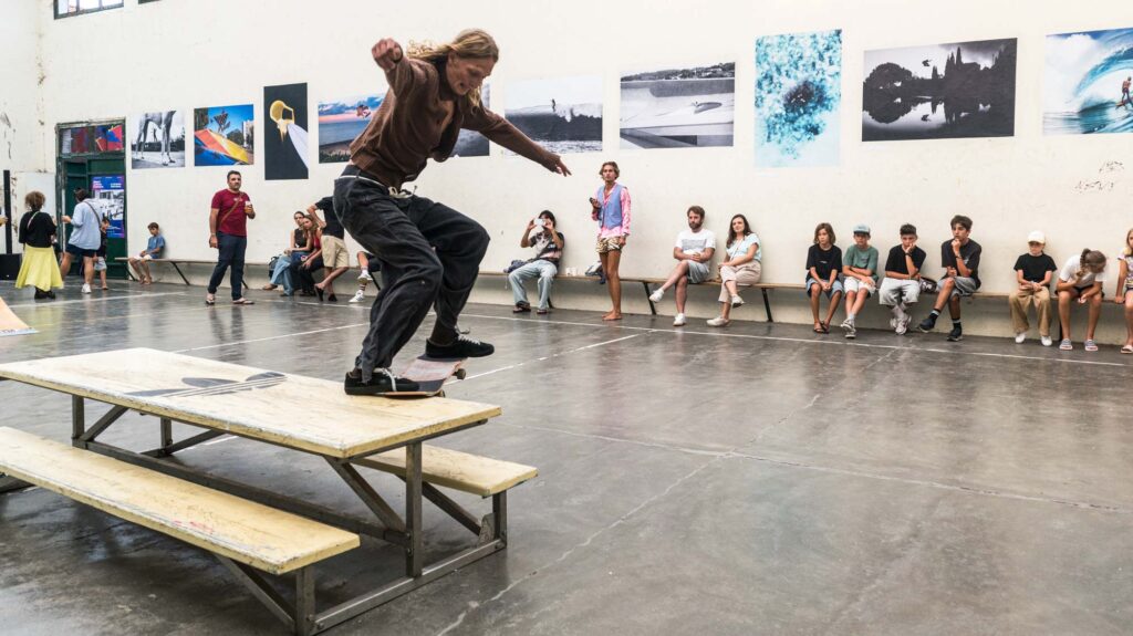 Skateur en figure sur une table de pique-nique, public assis devant les tirages exposés, Mur à Gauche Biarritz