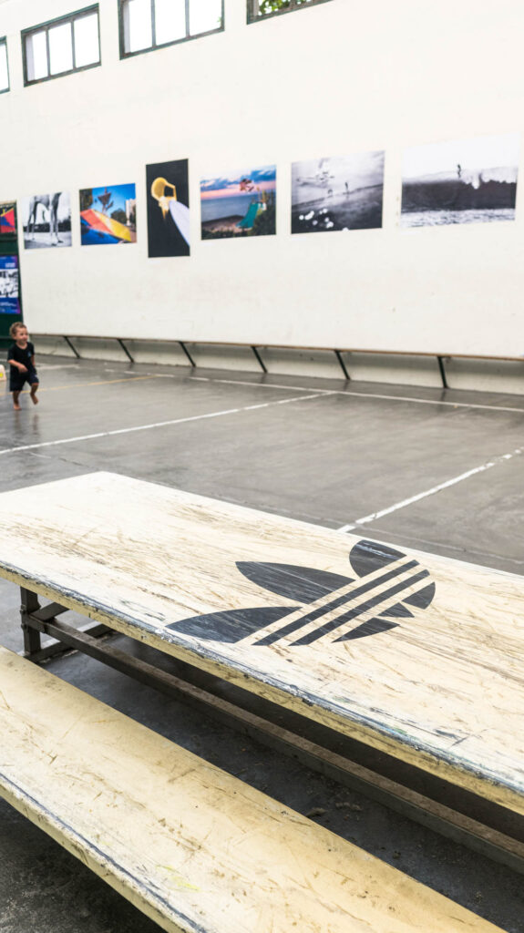 Table de skate avec logo Adidas au premier plan, tirages photo en fond, Summer Block Party, Biarritz